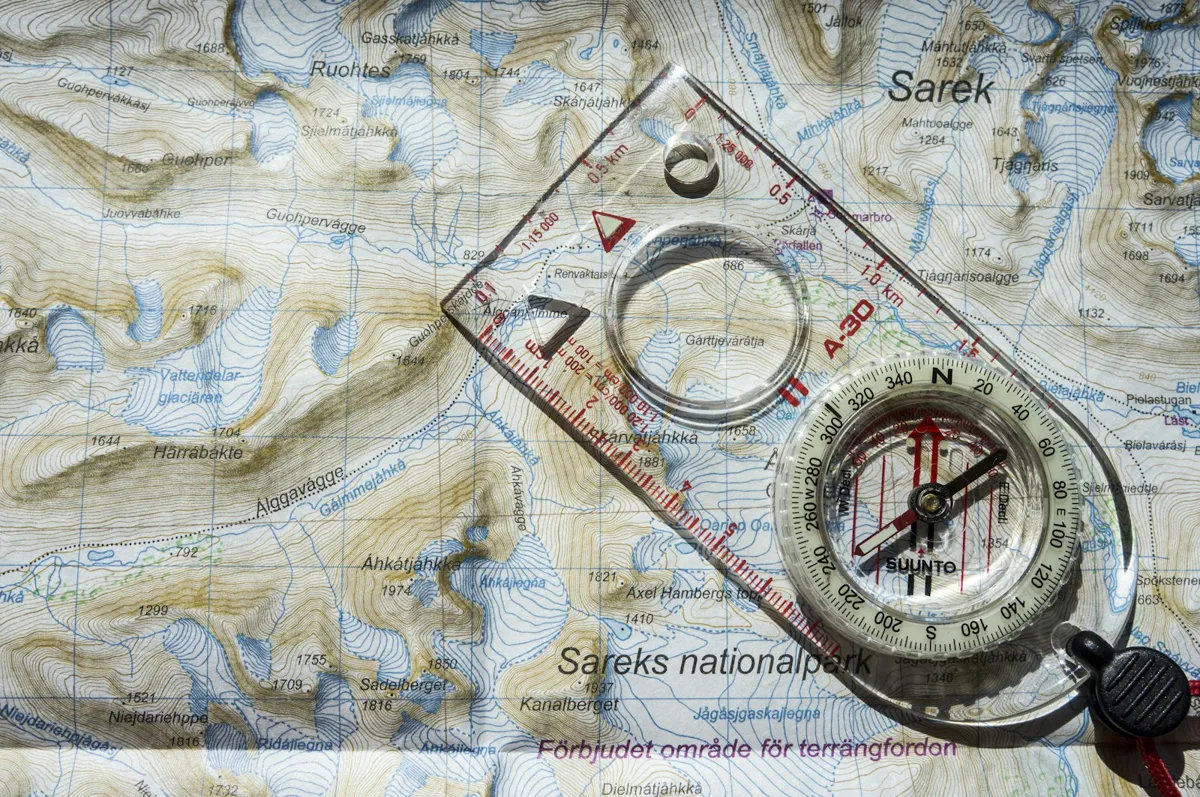 Kartenkompass mit Lineal liegt auf einer topografischen Wanderkarte