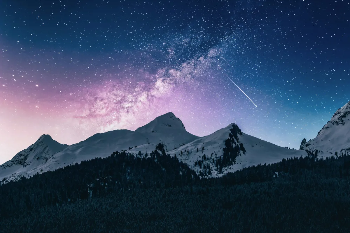 Milchstraße und Sternenhimmel über verschneiten Berggipfeln und dunklem Nadelwald